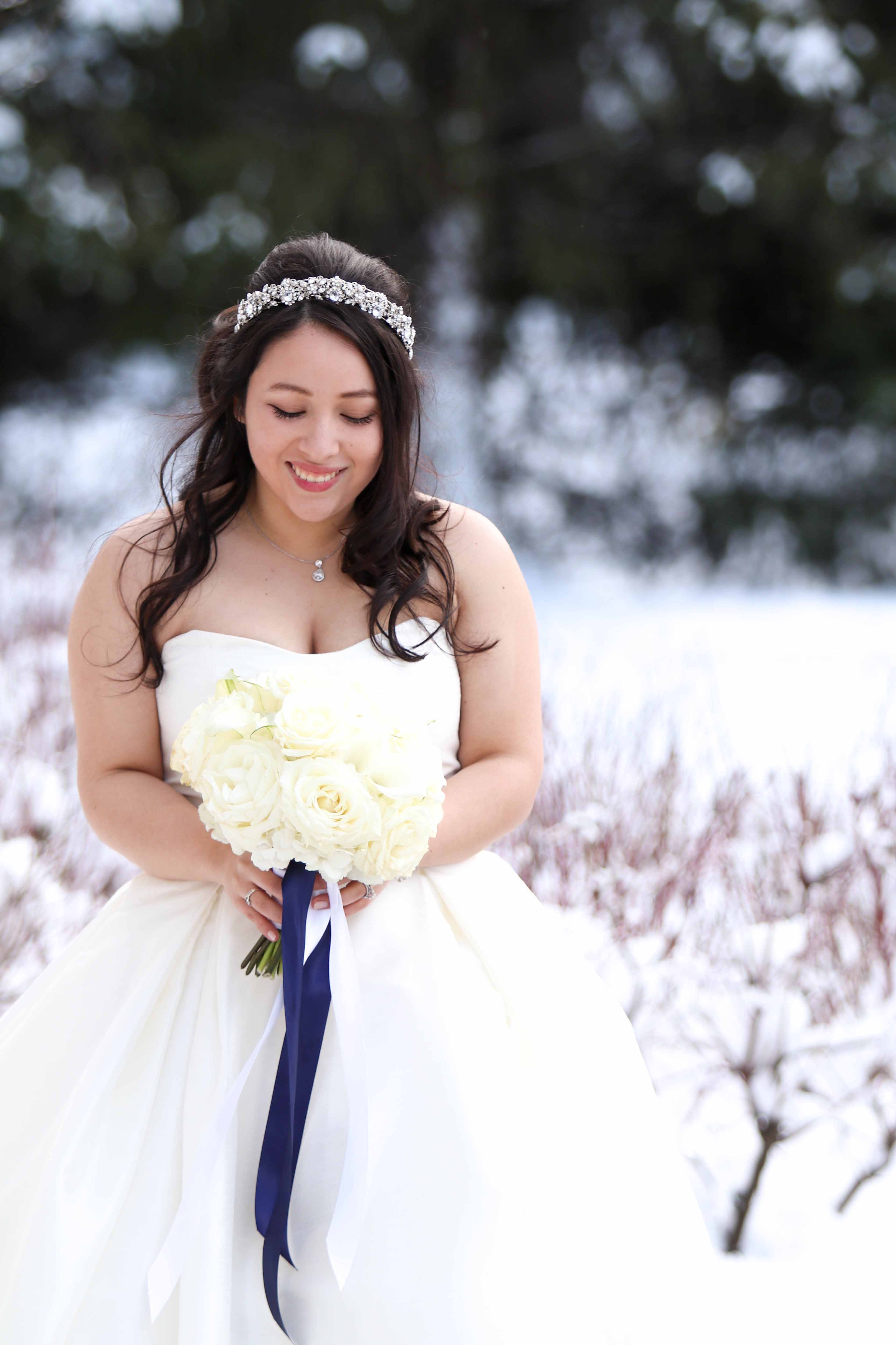 bride in white dress with white bouquet standing in snow