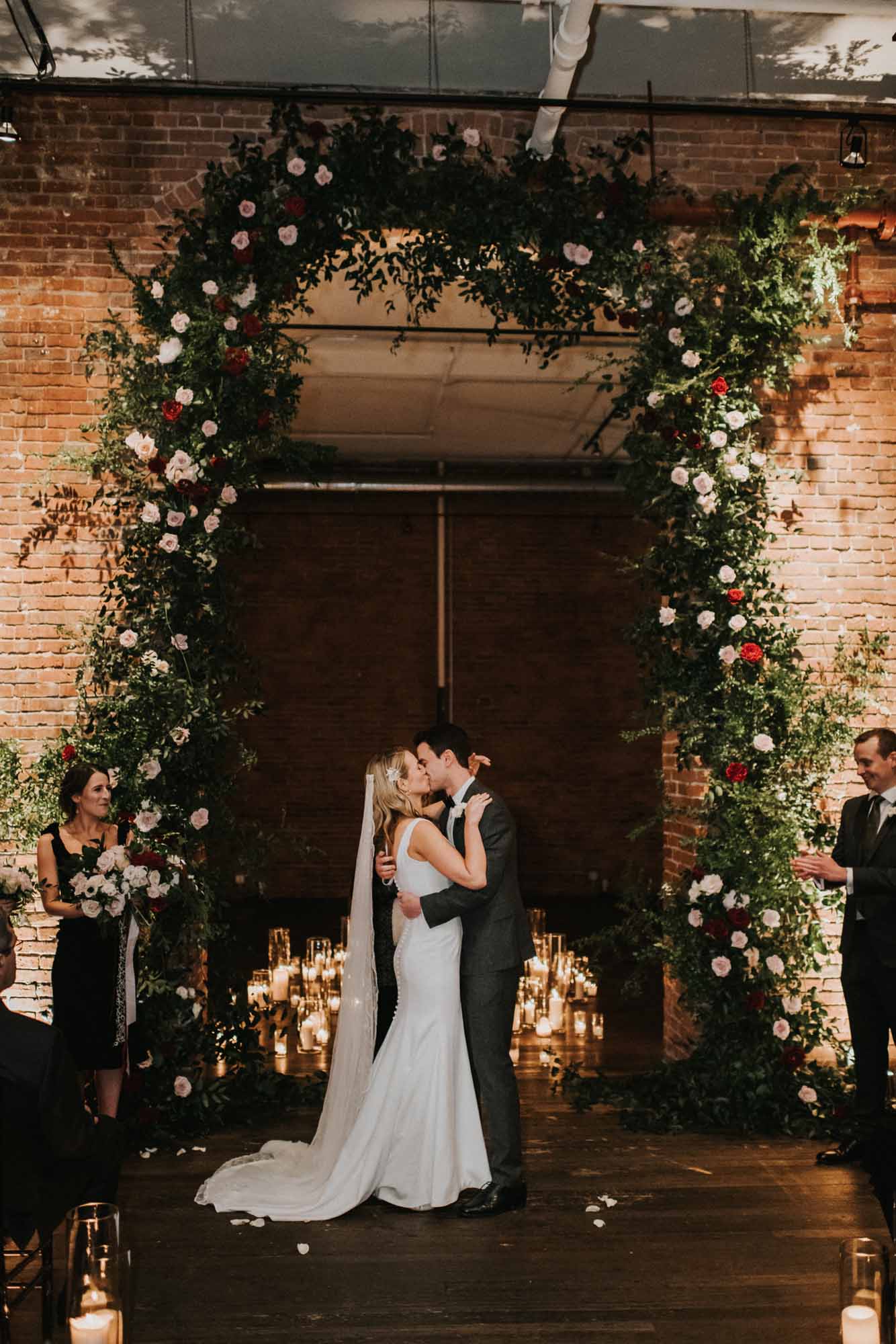 Bride and groom kiss under a tall floral arch at Axis Pioneer Square