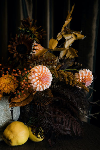 Fall texture in a Thanksgiving table centerpiece with peach dahlias, brown sunflowers, rust brown amaranthus, rosehops, and dried fern and fall foliage, with quince fruit