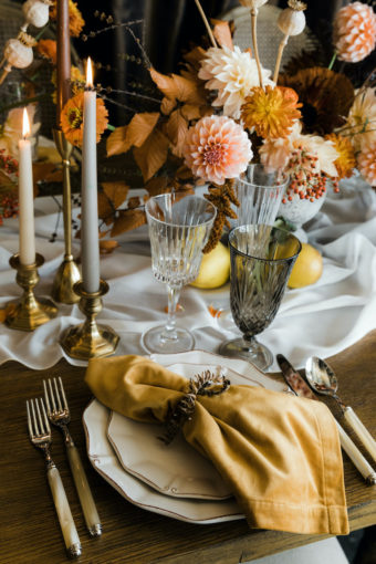 Wooden Thanksgiving table with sheer table runner, yellow velvet napkin, crystal cut glasses, taper candles, and flower centerpiece with orange dahlias