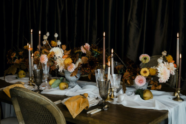 Thanksgiving table with fresh flower centerpieces containing peach colored dahlias, yellow zinnias, and fall textures, on wooden table with ivory sheer table runner, mustard yellow napkins, taper candles, Provence chairs - Decorating for the Holidays - FLORA NOVA DESIGN SEATTLE