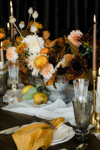 Floral centerpiece for Thanksgiving with orange and peach dahlias, dried poppy pods in stone vase with quince fruit and brown taper candles - Decorating for the Holidays - FLORA NOVA DESIGN SEATTLE