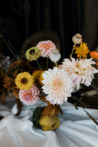 Thanksgiving centerpiece with peach dahlias, yellow zinnias, poppy pods, quince, on ivory sheer linen table runner