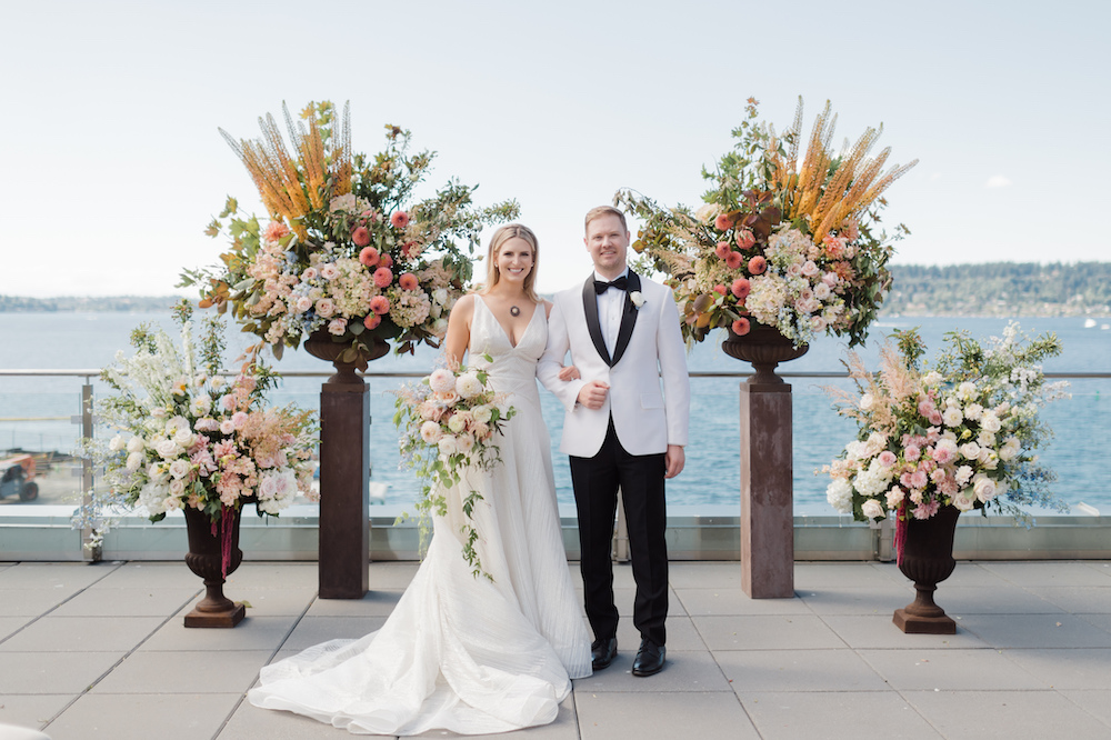 Bride and groom in front of their large floral ceremony backdrop for their Seattle outdoor wedding