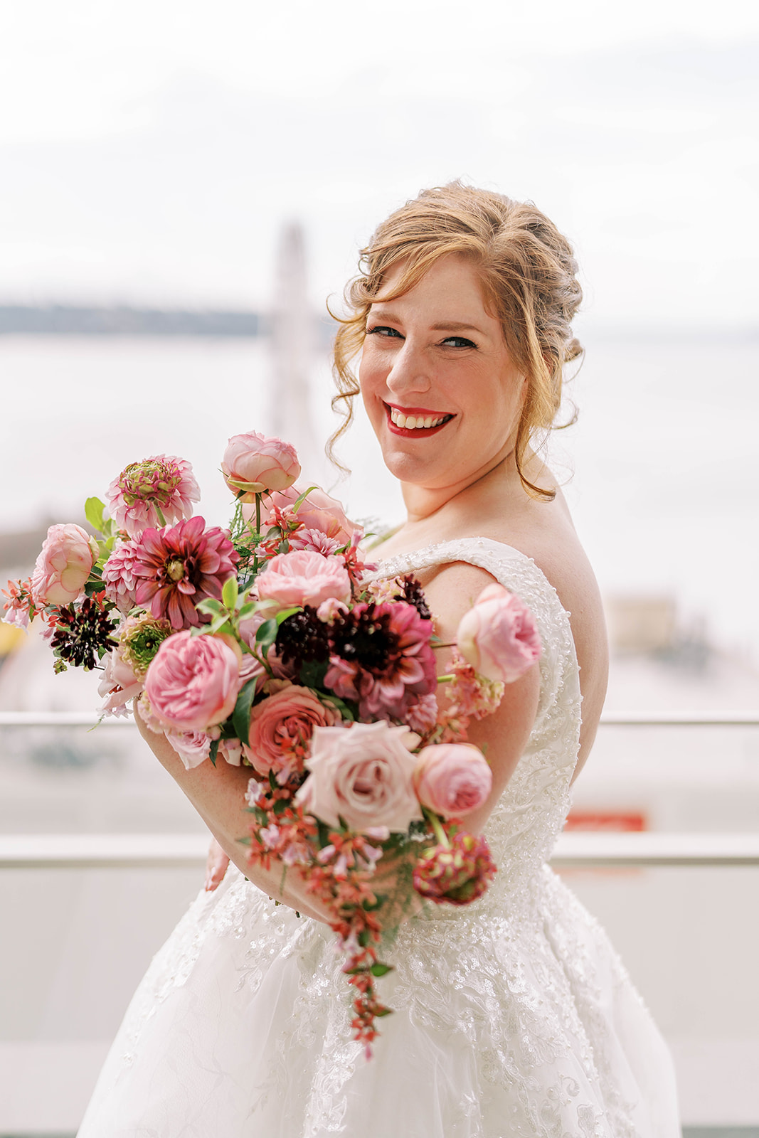 Bride smiles as she poses with her oval bridal bouquet in shades of pink flowers.