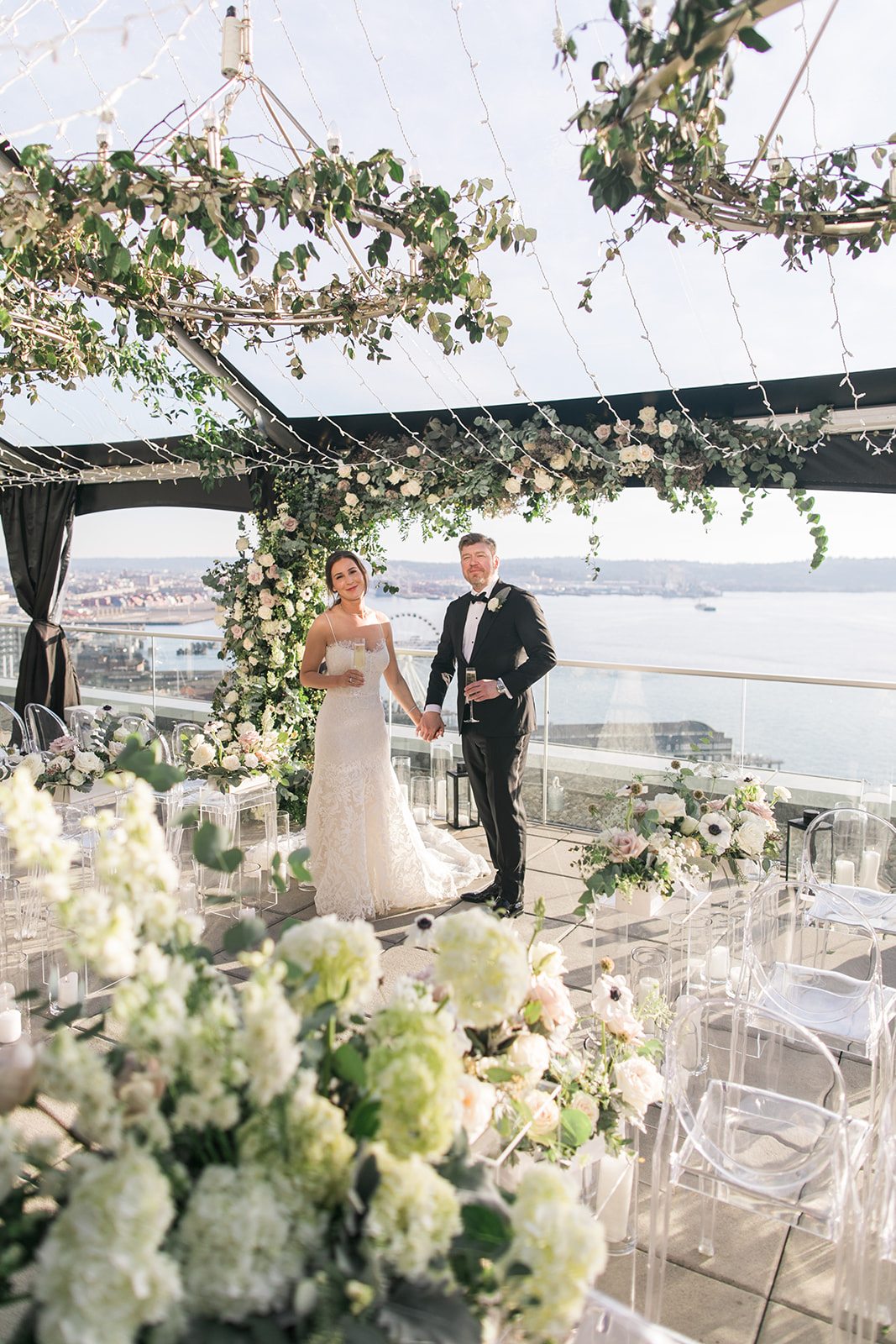 Bride and groom surrounded by white flowers and greenery on the rooftop of the Thompson Hotel Seattle with view of the Puget Sound