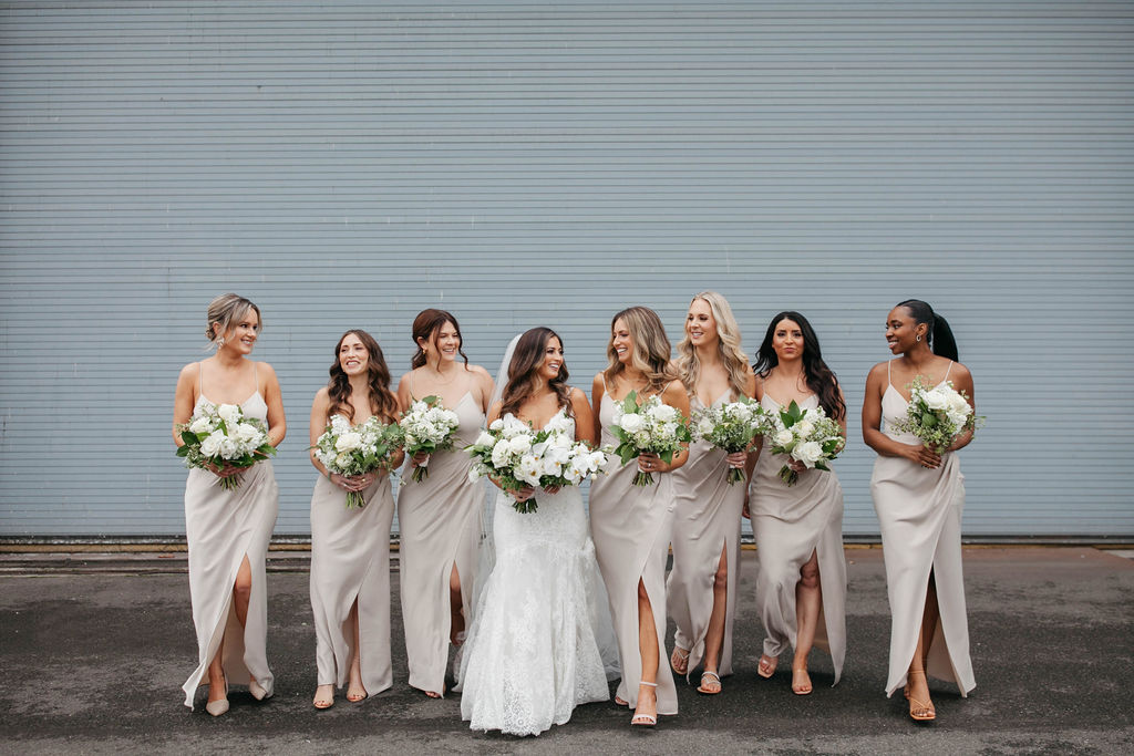 Bride and bridesmaids holding floral bouquets in white and green wearing champagne dresses