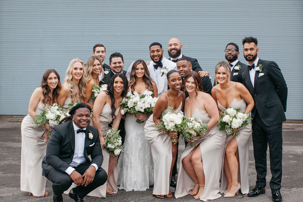 Wedding party with men in black suits and women in champagne dresses with white and green bouquets