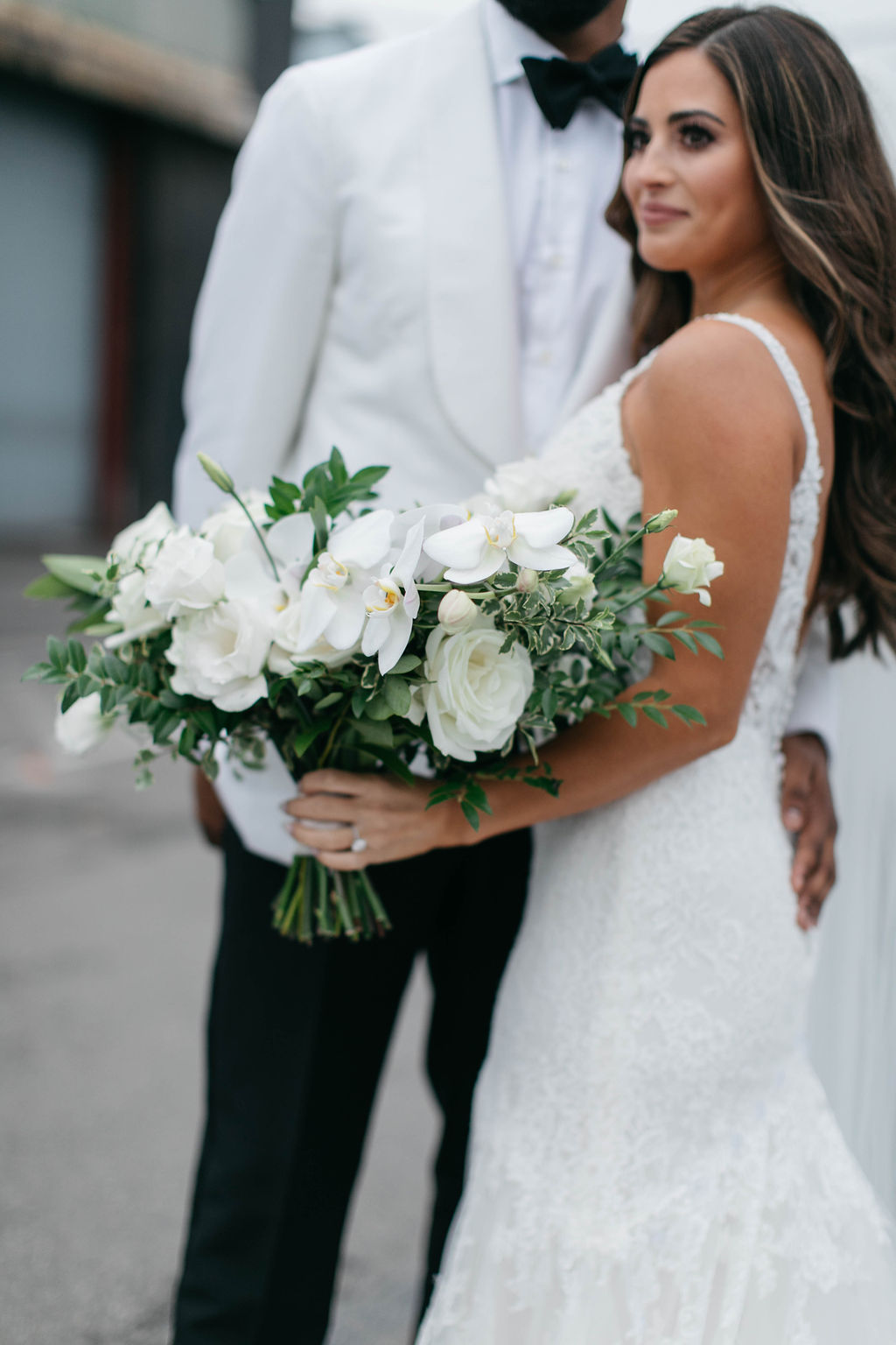 Bride holding bouquet of white phaleanopsis orchids, white roses, white lisianthus and greenery