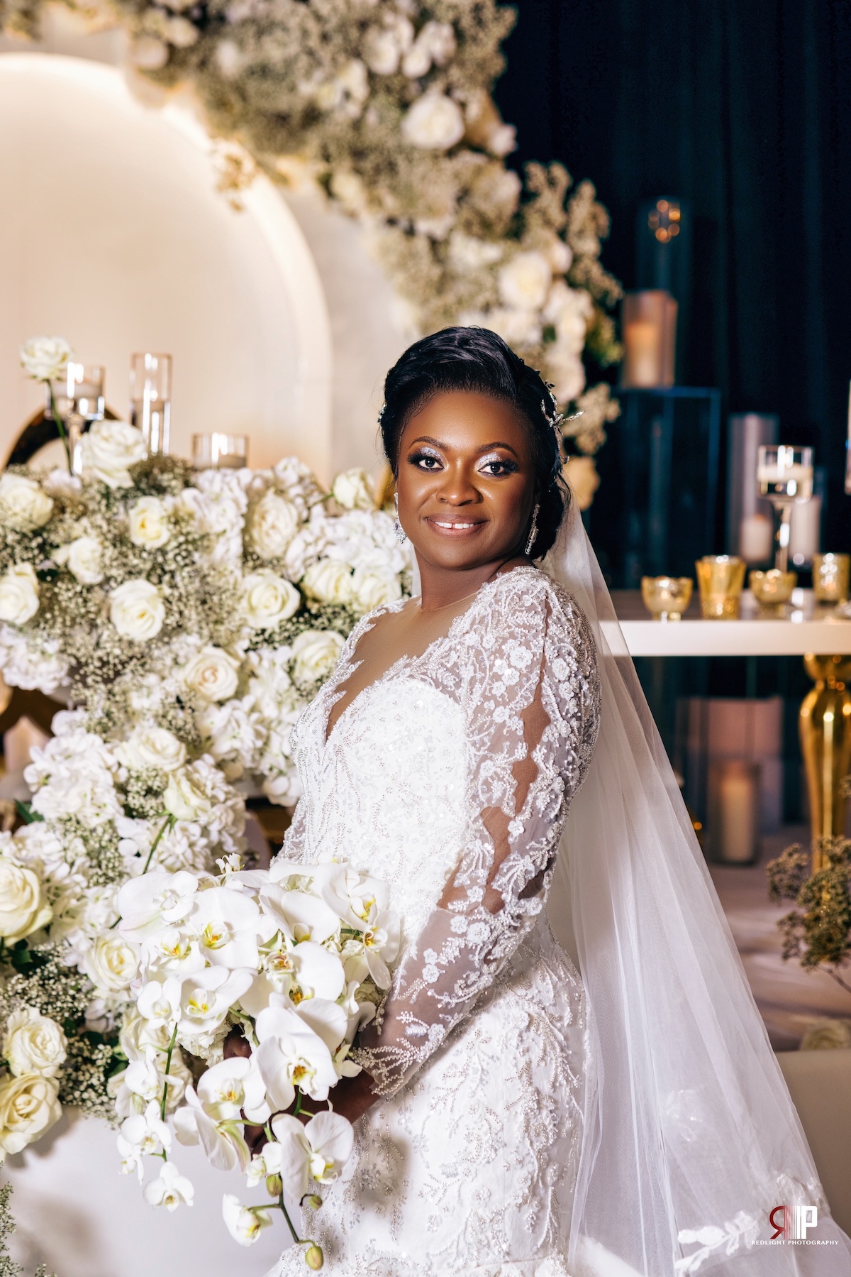 Bride stands with her bouquet full of orchids in front of the lushly designed head table.