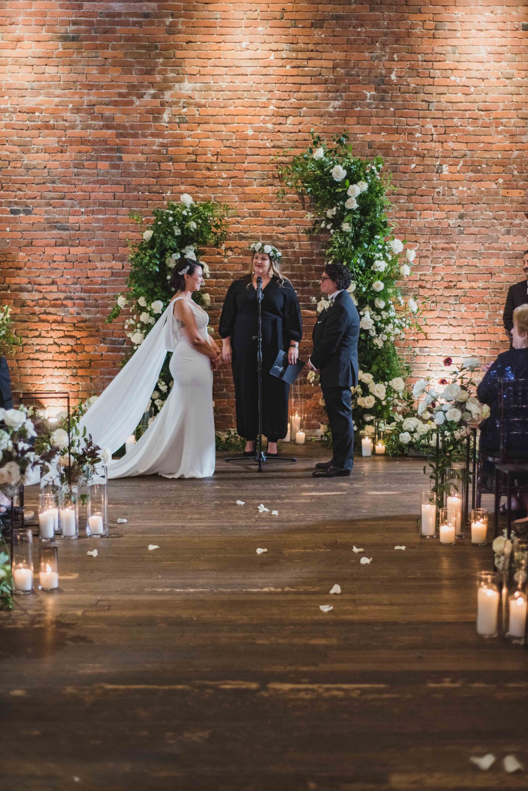 Brides stand during the ceremony in front of their lush floral and green arch designed by Seattle florist.