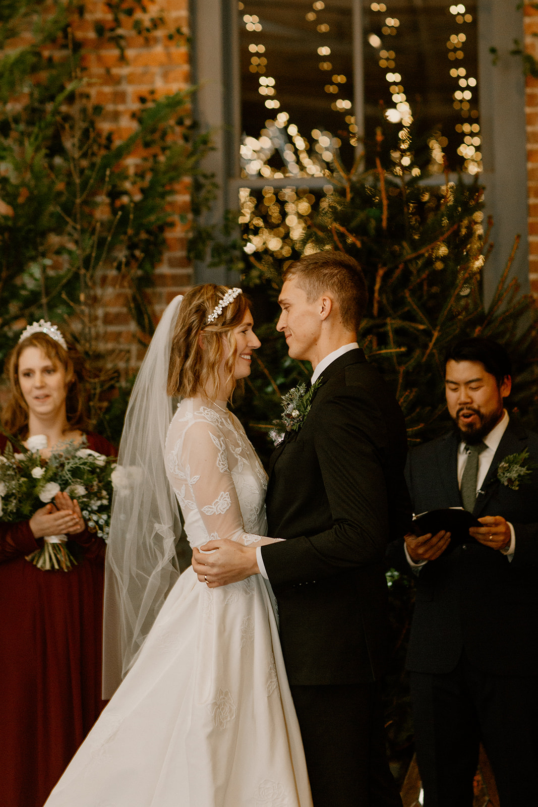 The bride and groom look into each others eyes during the ceremony with evergreen trees behind them.
