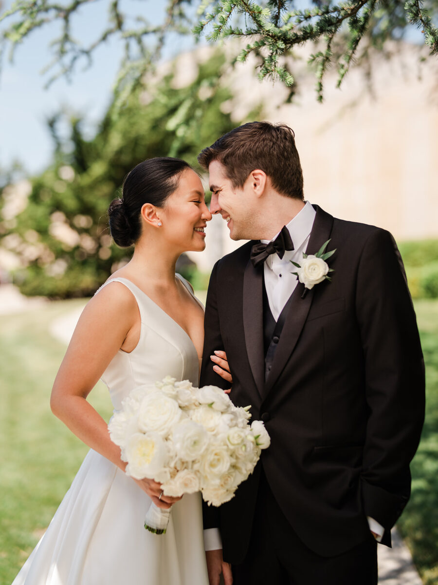 The bride and groom touch noses as the bride holds the lush white bridal bouquet designed by Flora Nova Design.