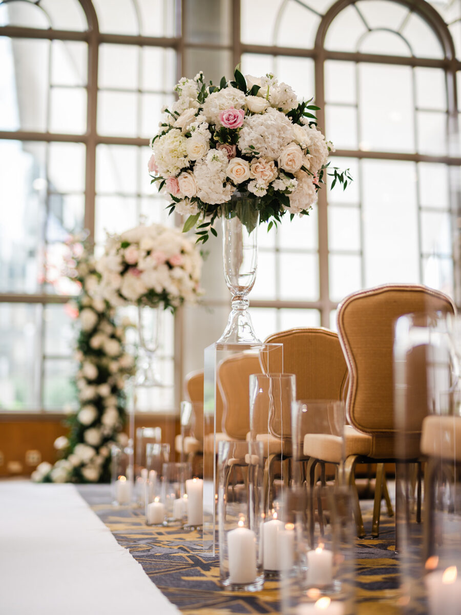 Charming tall white and blush arrangements on top of pedestals line the aisle along with candles.