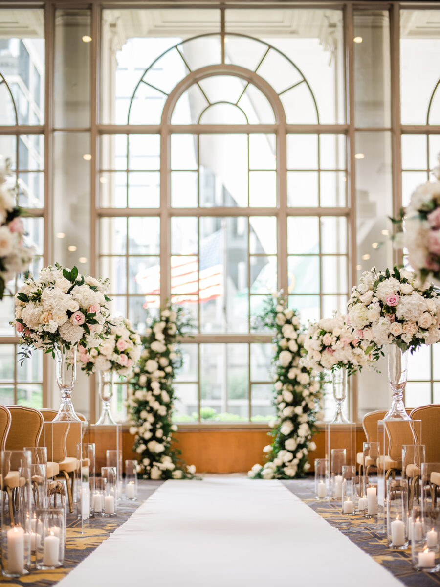 Tall and charming white and blush floral arrangements and candles fill the aisle.
