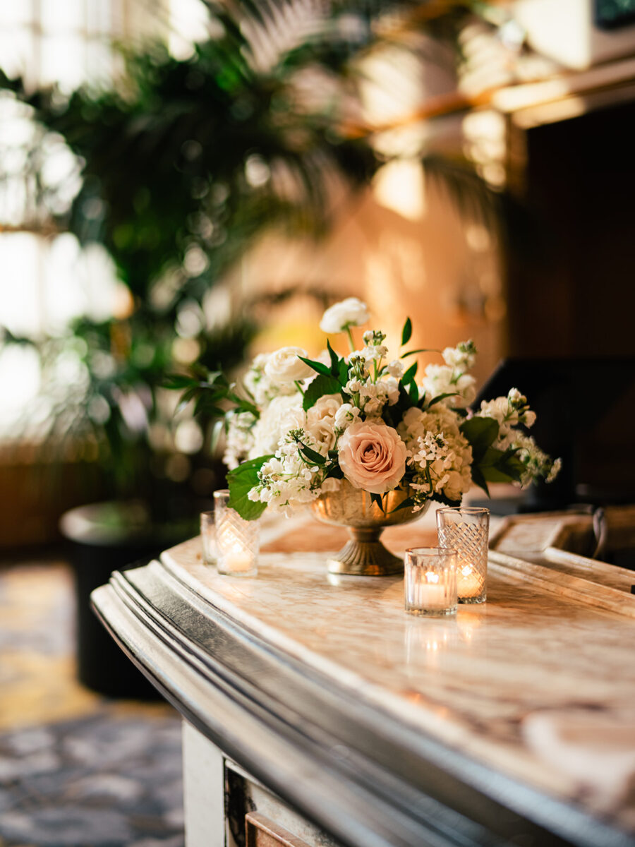 Charming blush and white floral arrangement in a golden vase and votive candles decorate the bar.