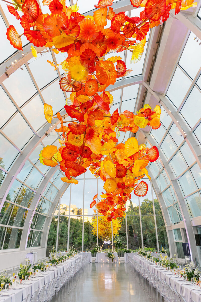 A whimsical moss garden wedding reception in the Chihuly Glass House is lined with tables decorated with lush and unique floral arrangements.
