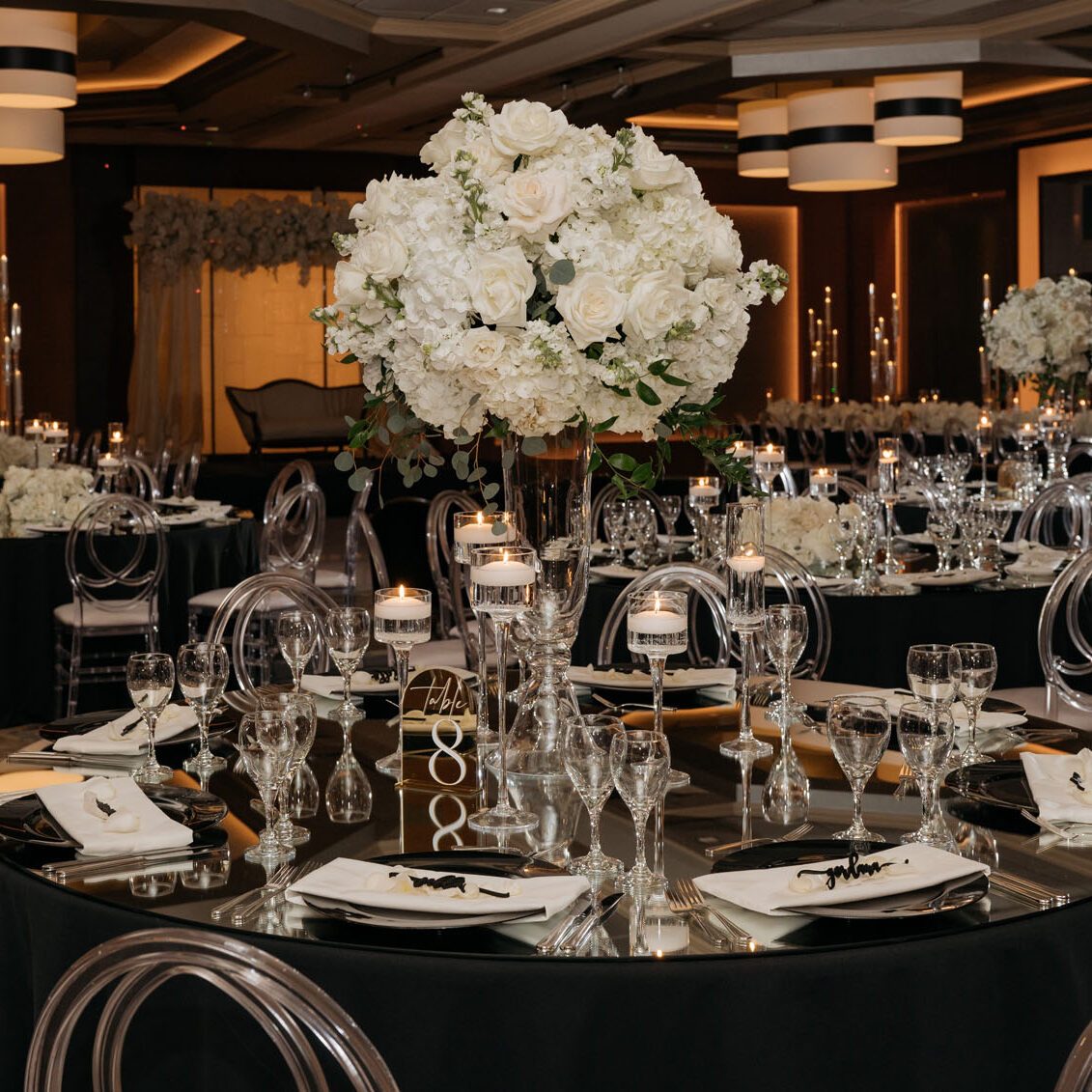A variety of vibrant tall and low white centerpiece poofs designed by Flora Nova decorate the black tables of the ballroom.