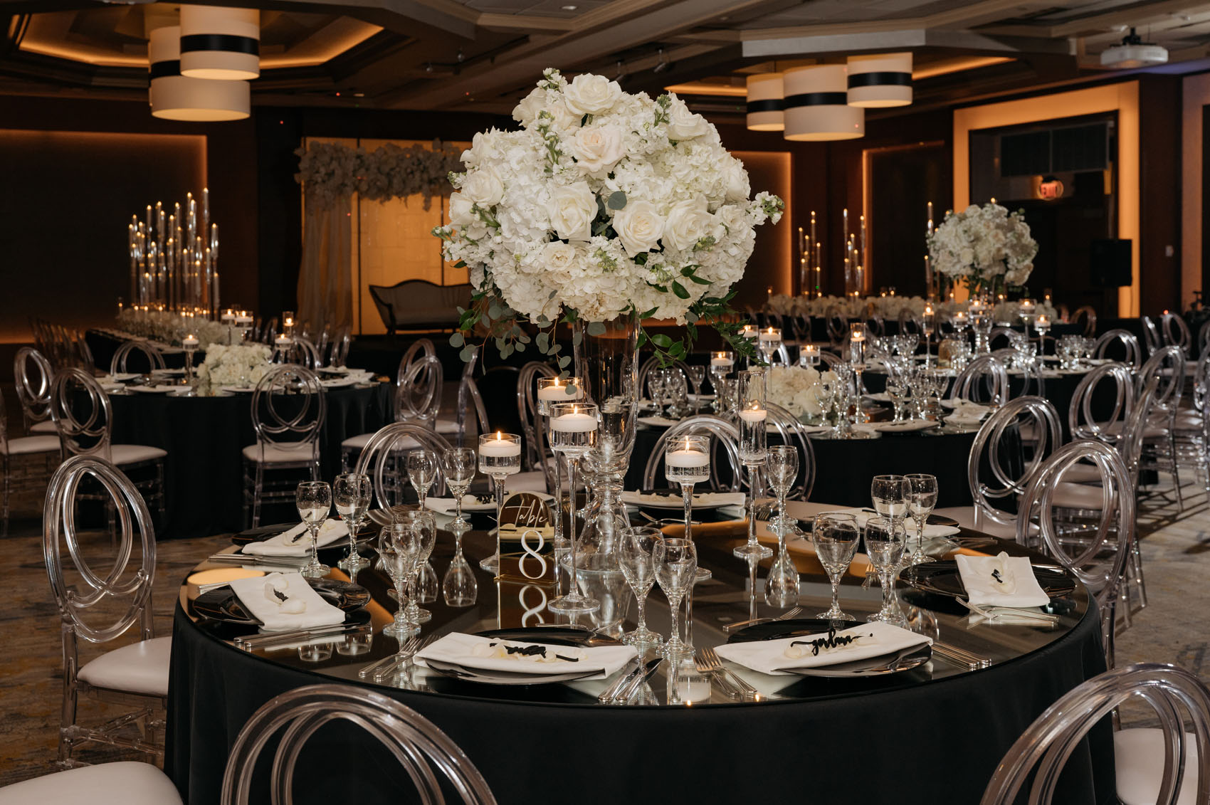 A variety of vibrant tall and low white centerpiece poofs designed by Flora Nova decorate the black tables of the ballroom.