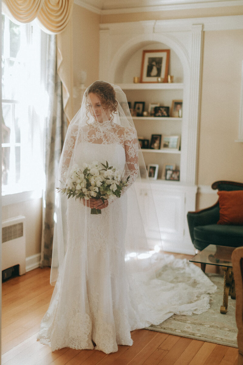 Bride holds her lush white bridal bouquet in The Admiral's House in her lace wedding dress.