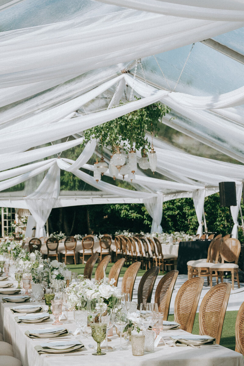 A timeless white wedding reception tent at The Admiral's House wis filled with tables lined with lush floral arrangements and antique tableware and ceiling installations.