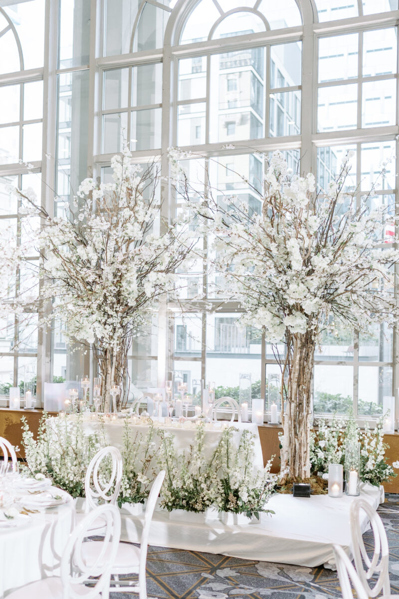 The sweetheart table is canopied between two cherry blossom trees and a meadow of lush floral arrangements designed by Flora Nova Seattle