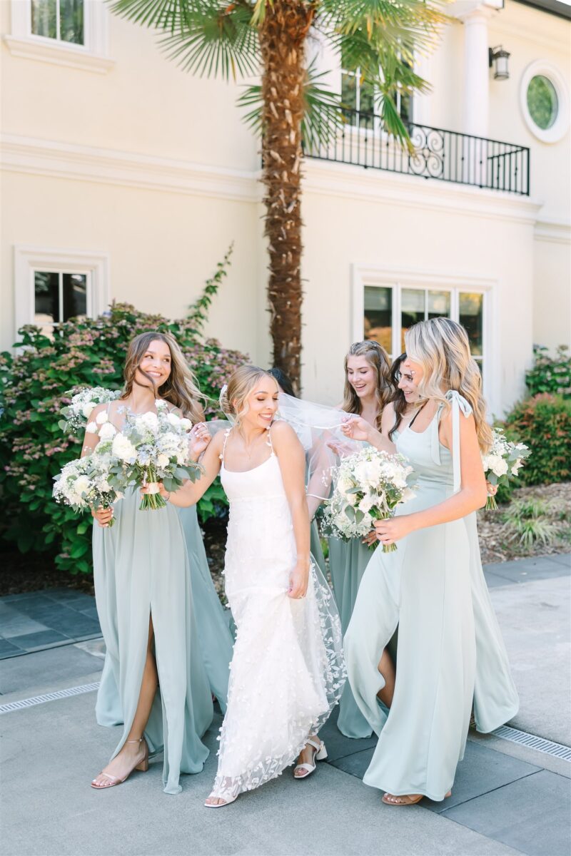 Bride and bridesmaids walk alongside each other carrying the brides veil while also holding their lush bouquets.