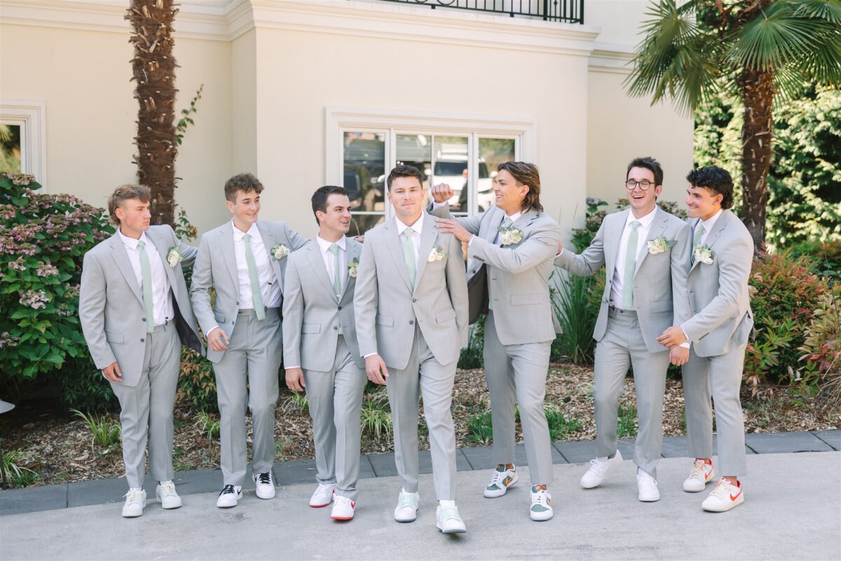 The groom and groomsmen all stand next to each other wearing their matching suits and boutonnieres.