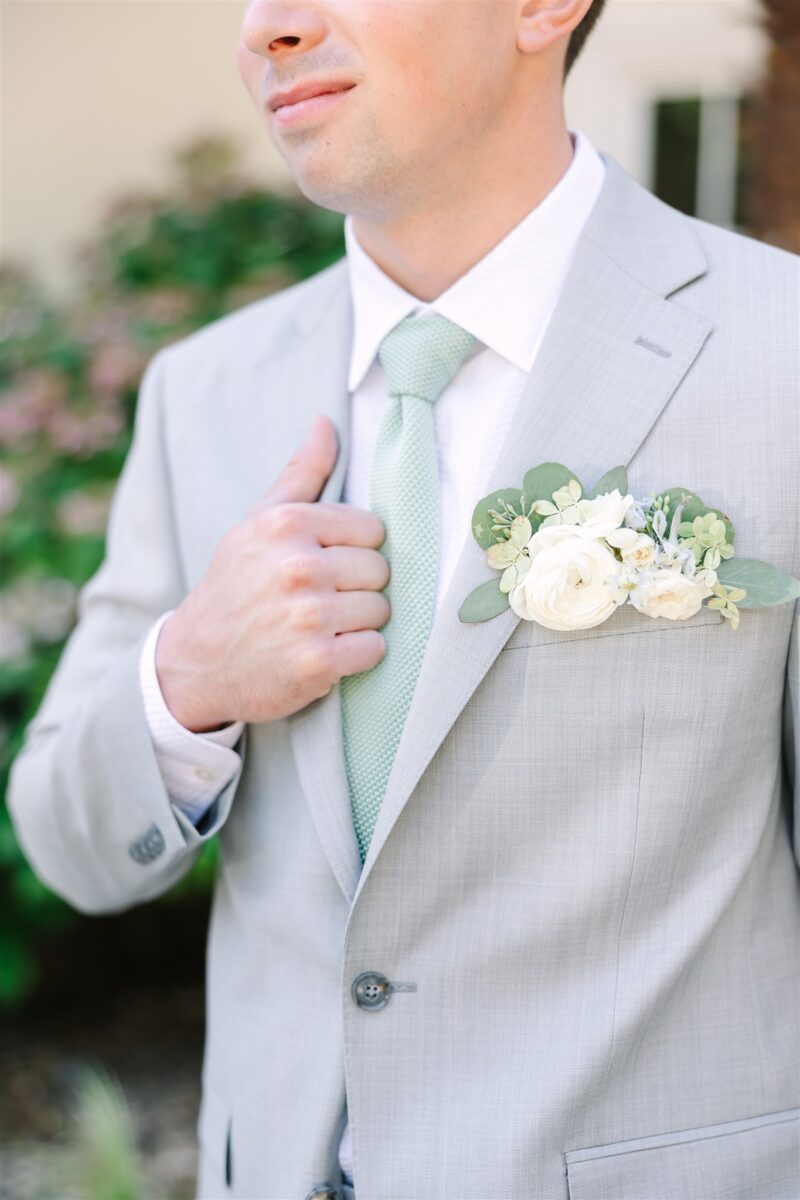 Groom wears a green tie that matches the white and green floral boutonniere with hints of blue.