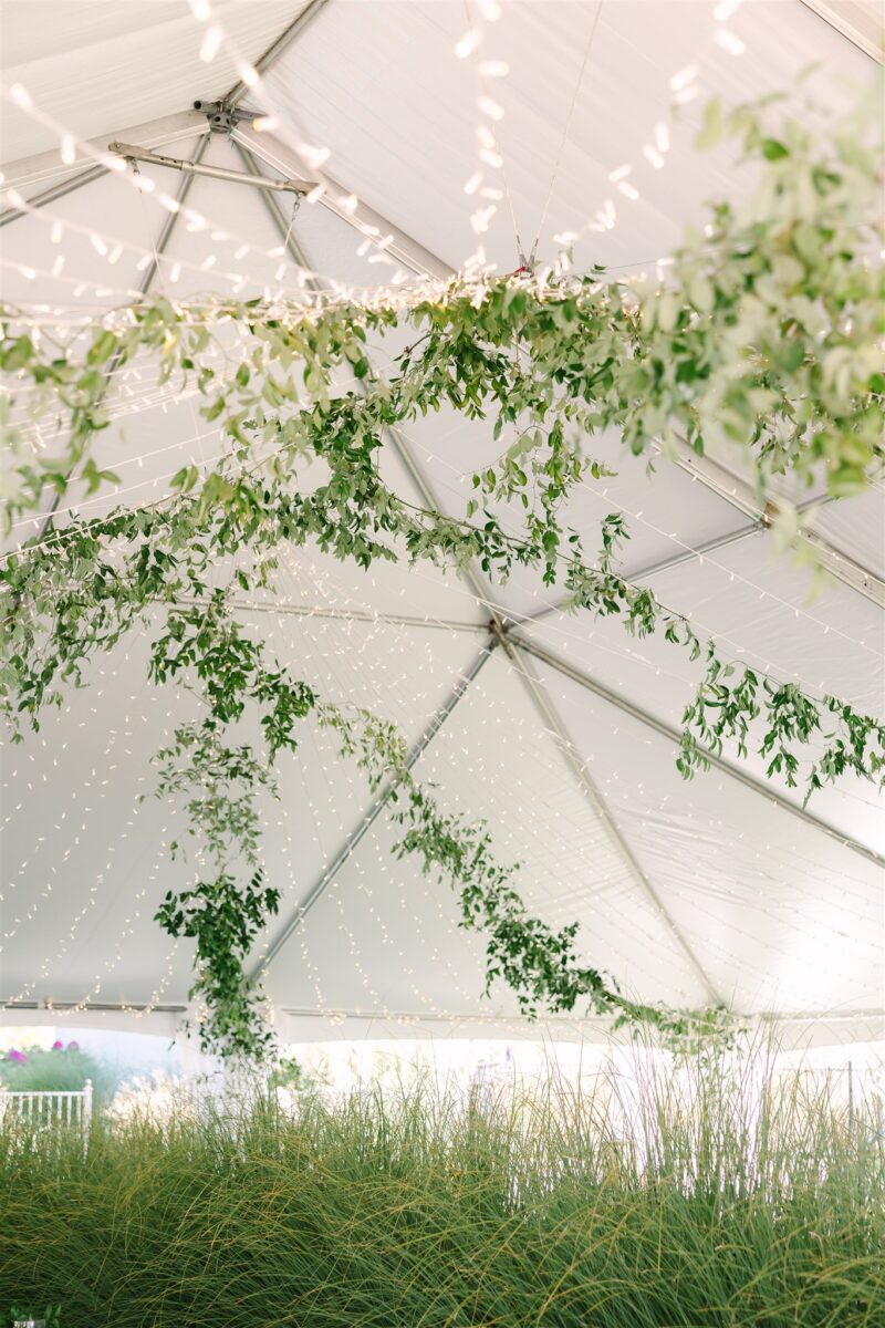 A large tent at the glamorous wedding at a private residence is decorates with fairy lights and greenery.