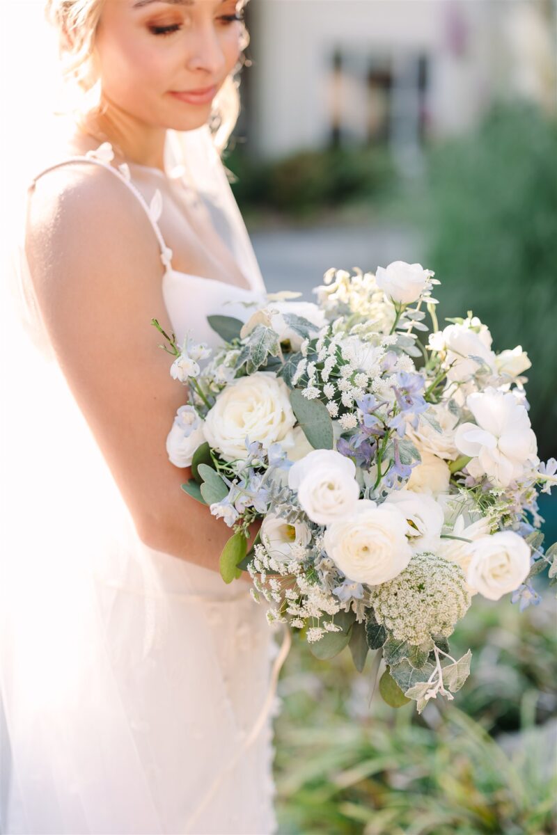 Stunning bride holds her lush white bridal bouquet with little peeks of her something blue.
