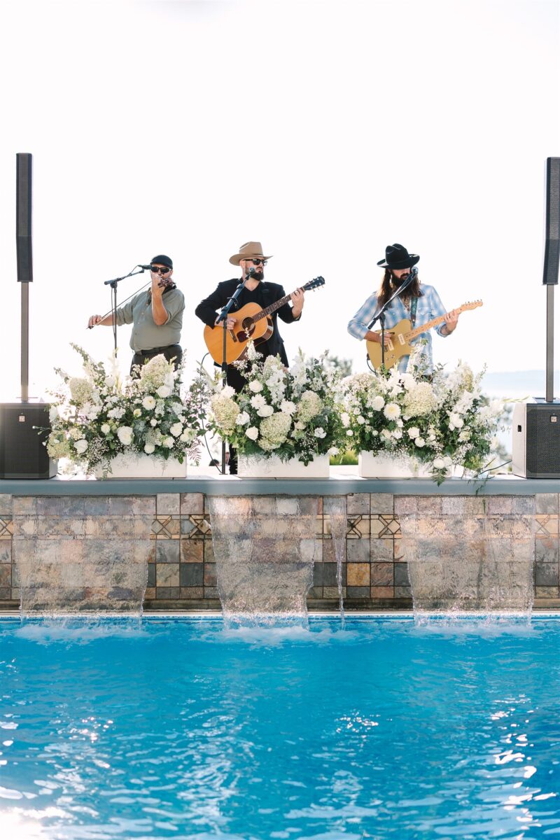 A band plays their music by the pool with floral arrangements about the waterfalls.