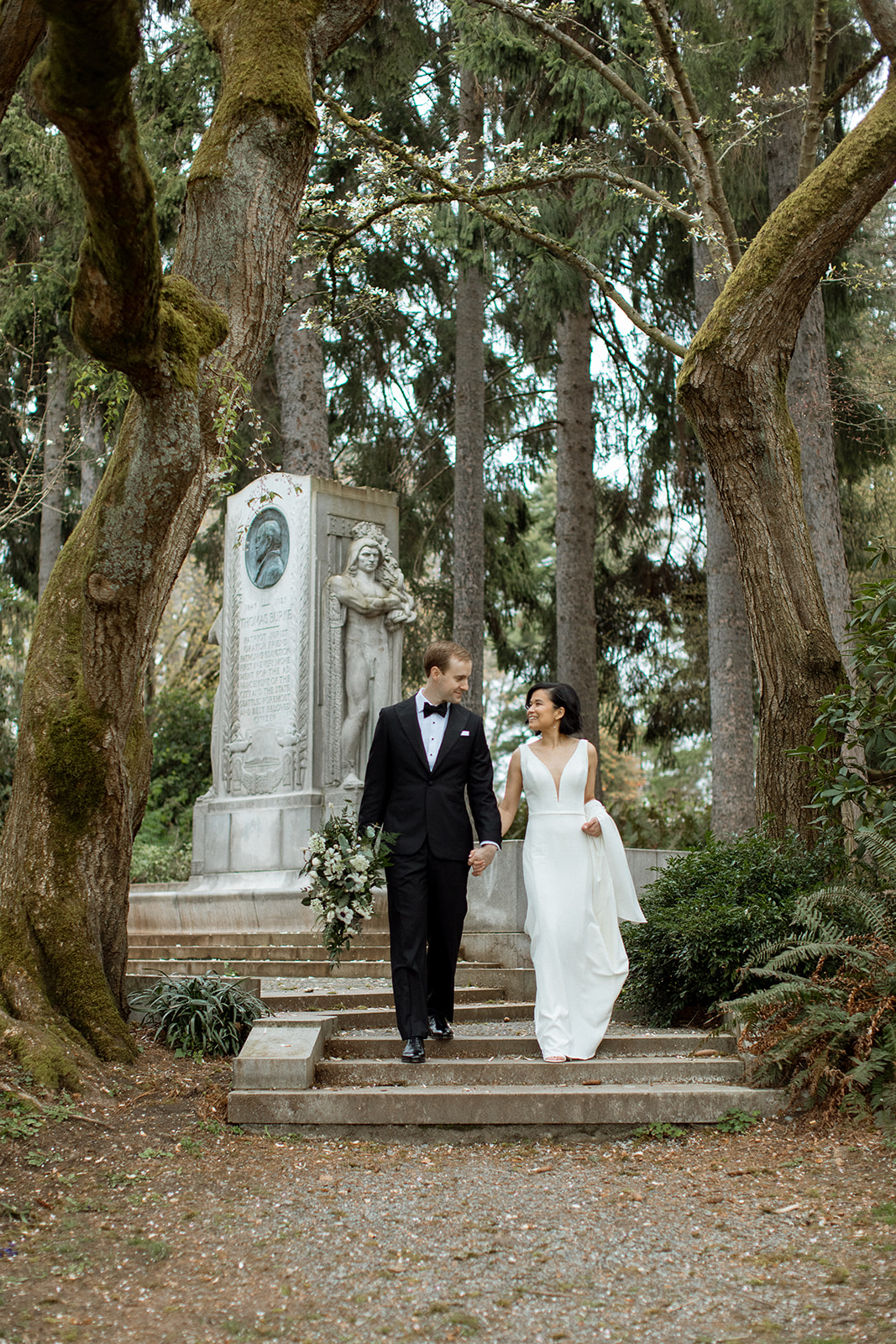 The groom holds the bridal bouquet in one hand and the brides hand in the other as they walk down the steps.