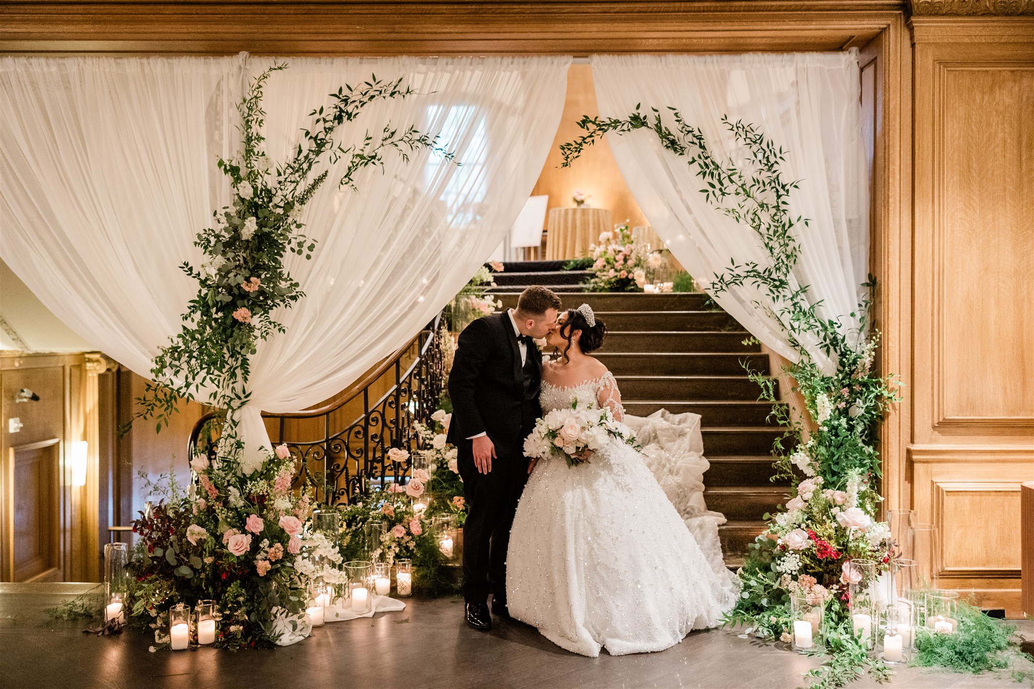 The bride and groom kiss under the draping and greenery of the Fairmont Olympic staircase