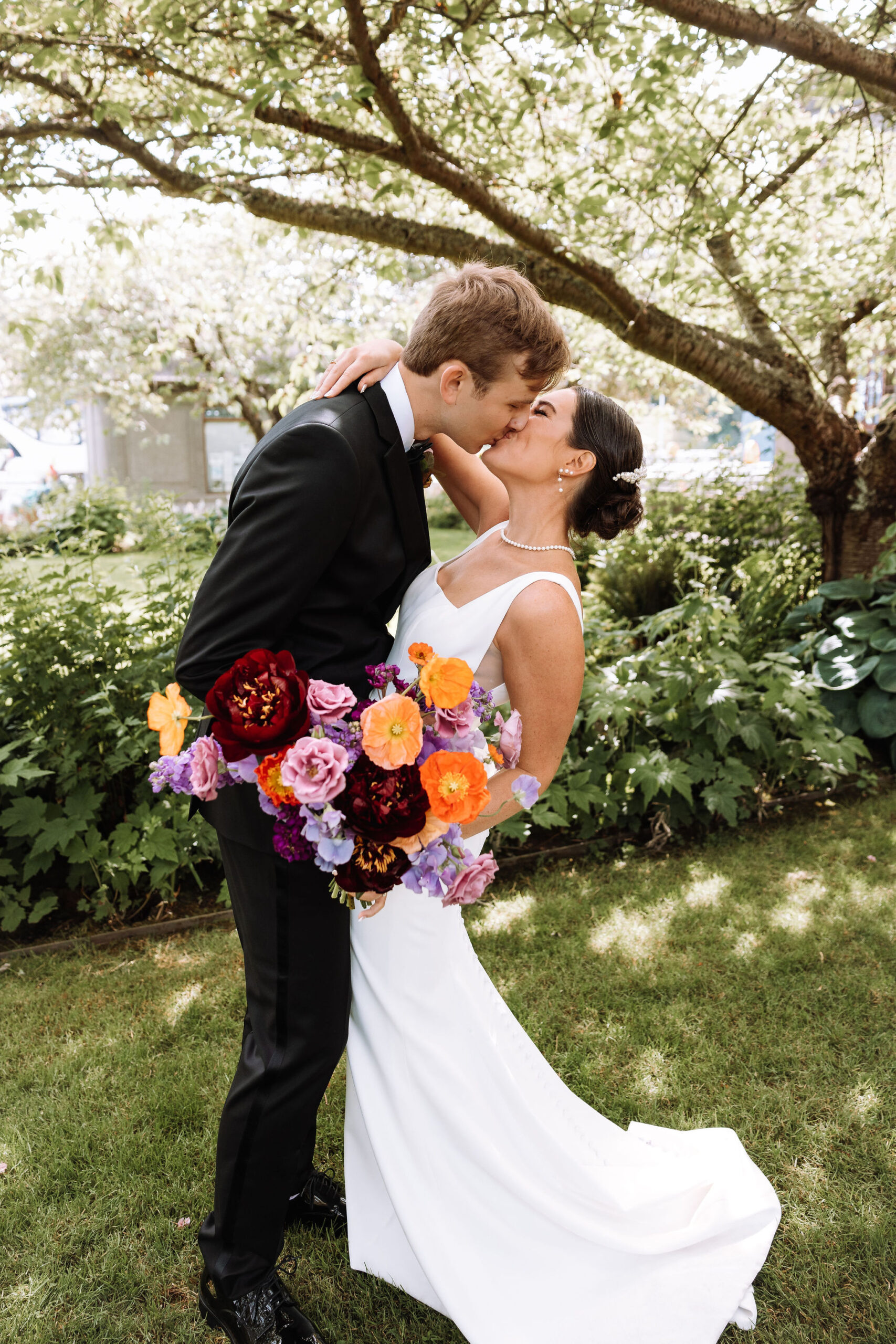 Intimate wedding kiss in lush garden with stunning bridal bouquet of seasonal blooms