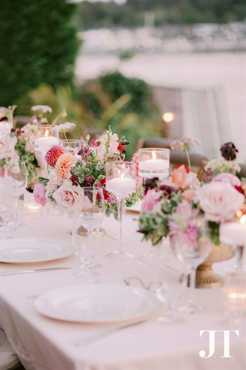Garden-style centerpiece arrangement with coral dahlias, burgundy scabiosa, and floating candles in brass compote creating intimate dining atmosphere