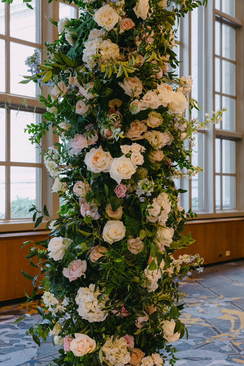 Dramatic ceremony arch detail showcasing an abundance of cream roses, white hydrangeas, and soft pink blooms with trailing greenery creating a romantic focal point