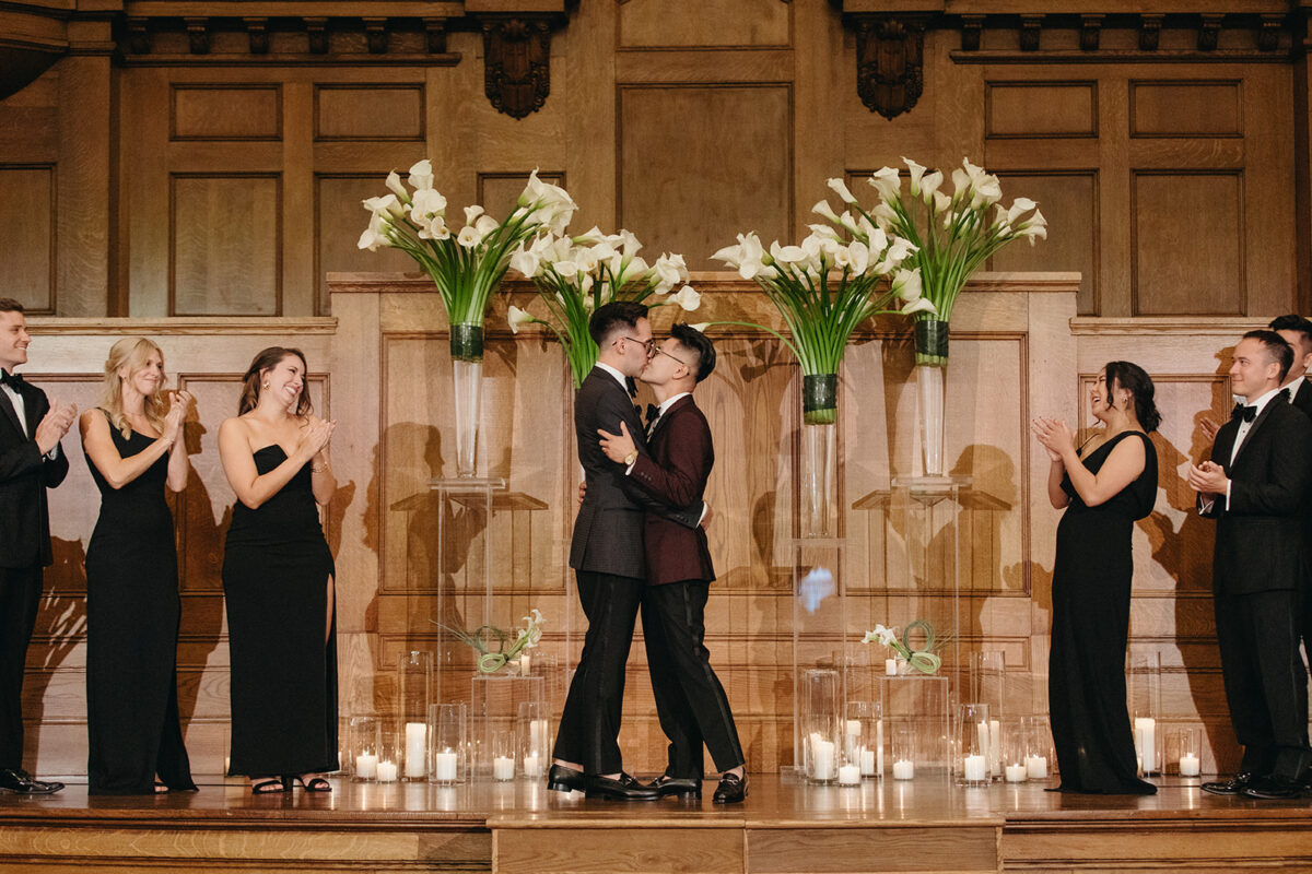 Two grooms sharing first kiss at altar surrounded by white calla lilies at Elegant Hotel Lotte Wedding