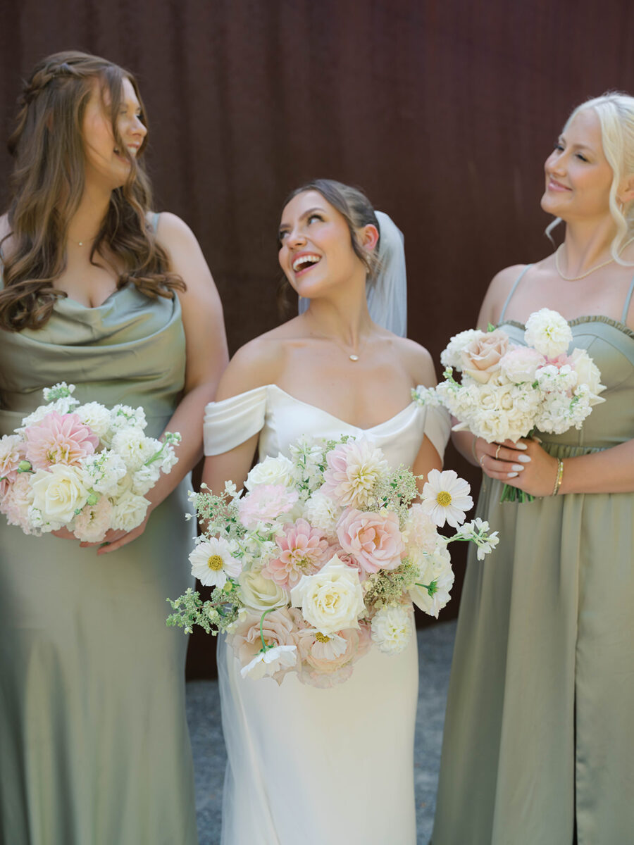 A Blush Summer Wedding in Seattle By Flora Nova Design bride holding soft blush and white bouquet with two bridesmaids in sage dresses holding smaller bouquets with roses, cosmos, dahlias and hydrangea.