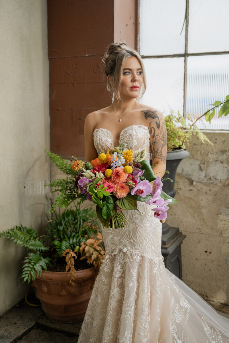 Beautiful Bride at The Ruins holding a colorful bridal bouquet with orange dahlias, lavender orchids, yellow craspedia, pink roses and lush greenery.
