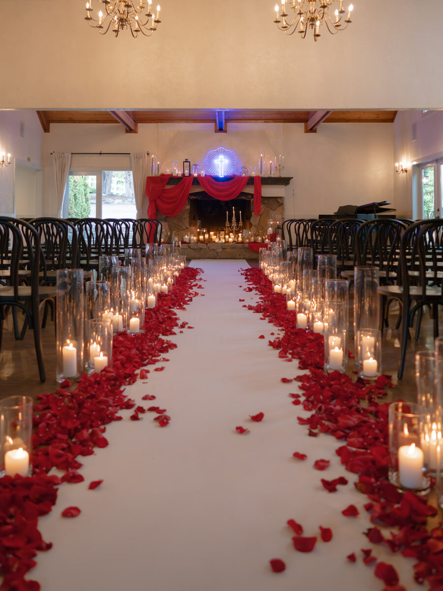 Theatrical wedding ceremony aisle lined with a thick layer of red rose petals and a collection of hurricane candles.