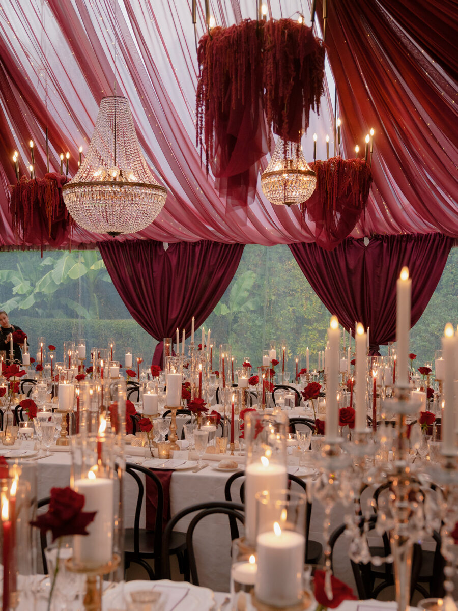 A reception with red amaranthus and crystal hanging chandeliers accenting a ceiling adorned with red drapery.