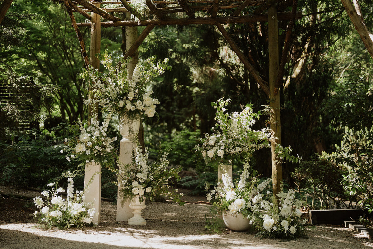 A wedding ceremony backdrop at a White Wedding at JM Cellars in Woodinville by Flora Nova Design. Highlighting white statement white floral arrangements.